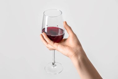 Gri arka planda kırmızı şarap bardağını tutan kadın.