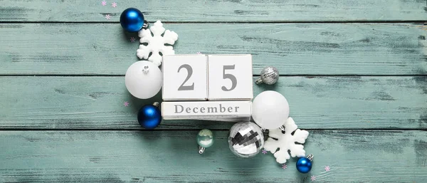 Christmas decorations and calendar with date DECEMBER, 25 on wooden background