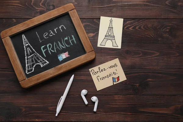 Chalkboard with text LEARN FRENCH, drawn Eiffel Tower, pen and earphones on dark wooden background