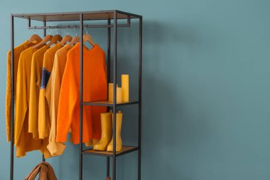 Giysileri, mumları ve mavi duvarın yanında ayakkabıları olan raf ünitesi.