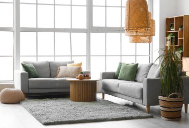 Işıl ışıl oturma odasının içinde rahat gri koltuklar ve yumuşak halıda kahve masası.