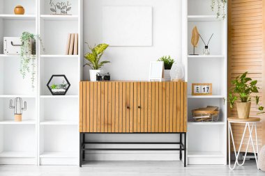 Odanın içinde ahşap dolap ve beyaz duvarın yanında raf üniteleri var.