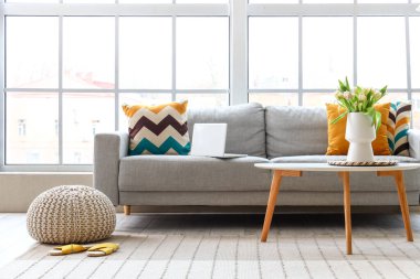 Büyük pencerenin yanında rahat bir kanepe ve sehpası olan parlak bir oturma odası.