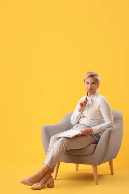 Not defterli olgun psikolog sarı arka planda koltukta oturuyor.