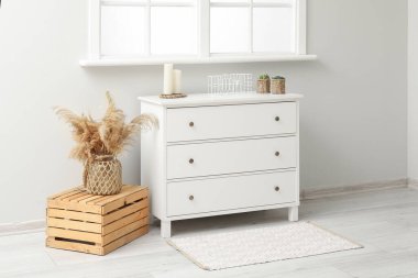 Pencere kenarındaki kutuda pampa otu olan beyaz çekmeceler ve vazolar.