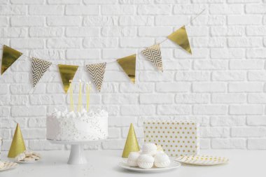 Doğum günü pastası, tuğla duvarın yanındaki beyaz masada mumlar ve şekerler.