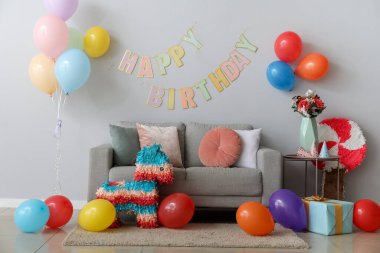 Doğum günü için dekore edilmiş oturma odasının içinde balonlar, pinatalar ve çelenkler var.
