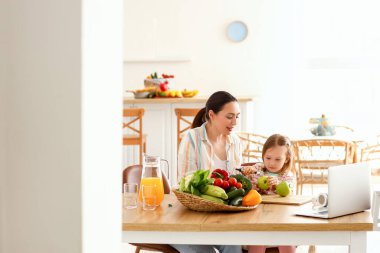 Annesi mutfakta elma soyan küçük bir kız.