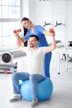 Genç adam rehabilitasyon merkezinde dambıl ve fizyoterapist eğitimi alıyor.