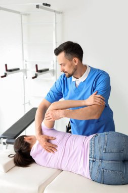 Rehabilitasyon merkezinde genç bir kadınla çalışan erkek fizyoterapist.