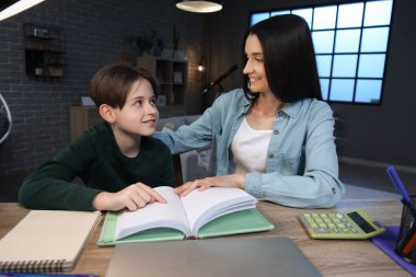 Anne ve küçük oğlu akşam geç saatte masada oturup kitap okuyorlar.