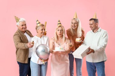 Pasta ve şampanyayla olgun insanlar pembe arka planda doğum gününü kutluyorlar.