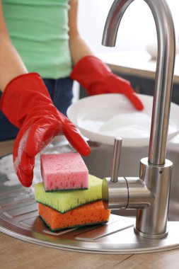 Kırmızı lastik eldivenli bir kadın bulaşıkları süngerle yıkıyor.