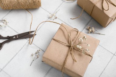 Beyaz fayans zemininde makas, iplik ve kurumuş dallarla bağlanmış kutular