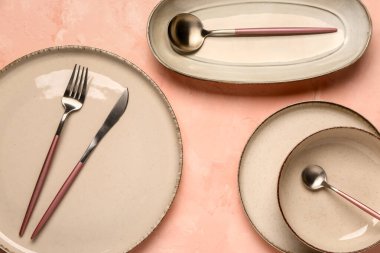 Pembe masada temiz tabak, kase ve çatal bıçak takımı var.