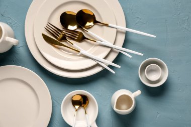 Mavi grunge masasında altın çatal bıçak takımı olan temiz tabaklar.