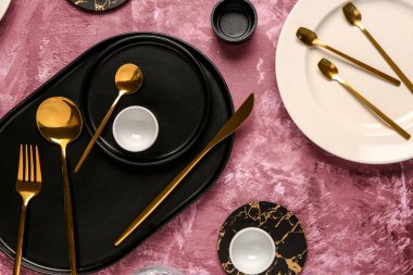 Koyu pembe masa üzerinde altın çatal bıçak takımı olan temiz tabaklar.