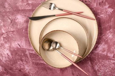 Koyu pembe masada temiz tabak, kase ve çatal bıçak takımı.