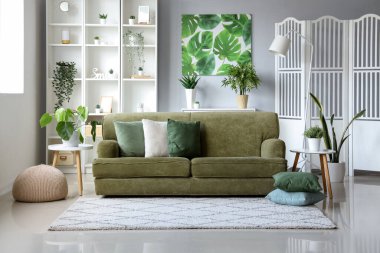 Yeşil kanepe ve çiçeklerle aydınlık oturma odasının içinde.