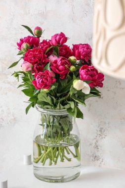 Bej grunge duvarının yanında kırmızı şakayıklı vazo