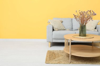 Kanepenin yanındaki kahve masasında kurumuş çiçek vazosu.