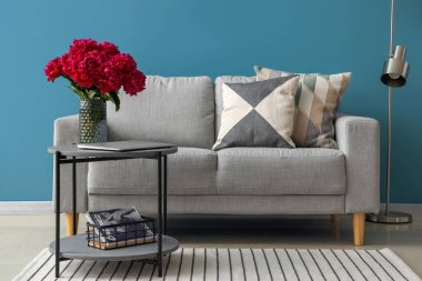 Kahve masalı kırmızı şakayık vazosu, kanepe ve mavi duvarın yanındaki lamba.