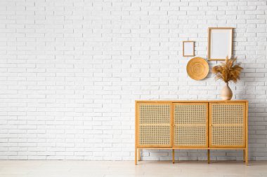 Çimenli modern çekmeceler ve odadaki açık tuğlalı duvarda asılı boş resimler.