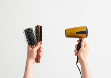 Beyaz arka planda fırça ve saç kurutma makinesi olan erkek eller.