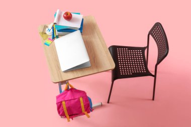 Sırt çantası, dizüstü bilgisayarı ve pembe arka planı olan modern okul masası.