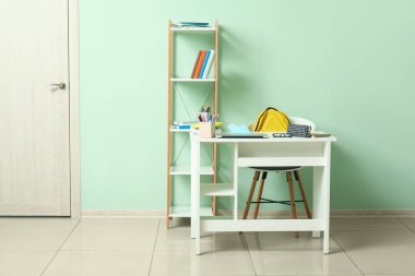 Sırt çantası, laptop ve kırtasiyeli modern okul masası yeşil duvarın yanında.