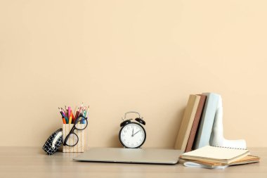 Bej duvarın yanındaki odada dizüstü bilgisayarı, çalar saati ve kırtasiyesi olan modern okul masası.