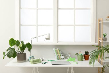 Laptop ve kırtasiyeli modern okul masası beyaz duvarın yanında.