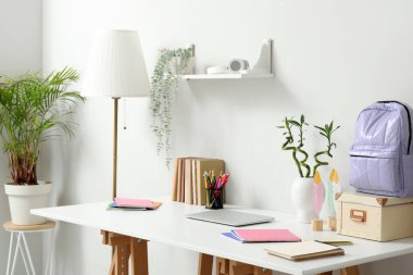 Laptop ve kırtasiyeli modern okul masası beyaz duvarın yanında.