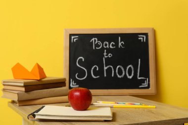 Modern okul masası, kırtasiye ve karatahta. Sarı duvarın yanındaki odada okula dönüş yazısı var.