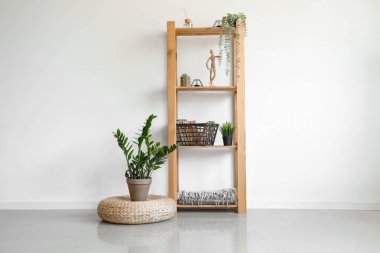 Beyaz duvarın yanında sepet, dekor ve çiçek bulunan raf ünitesi.