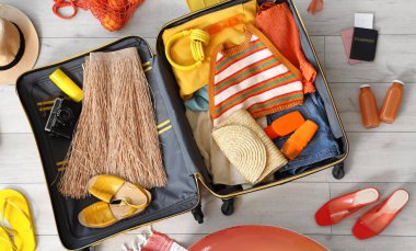 Plaj aksesuarlarıyla birlikte açık bavul. Açık ahşap zemin, üst manzara.