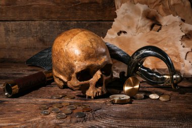 Kahverengi ahşap arka planda dürbünlü, kılıçlı, pusula ve bozuk paralı insan kafatası.