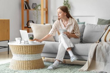 Tablet bilgisayarı ve dizüstü bilgisayarı olan genç bir kadın evde çalışıyor.