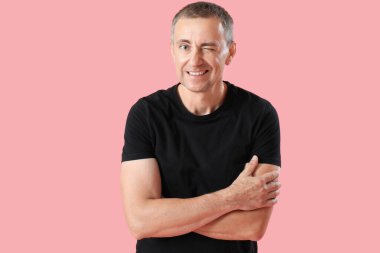 Pembe arka planda çapraz kolları olan olgun bir adamın portresi.