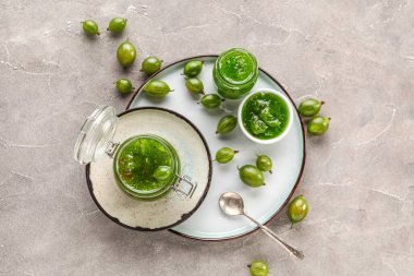 Gri arka planda lezzetli bektaşi üzümü reçeli olan kavanoz ve kase.