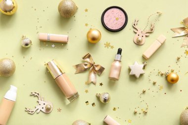 Dekoratif kozmetik ürünleri ve açık sarı arka planda altın Noel dekoru olan kompozisyon