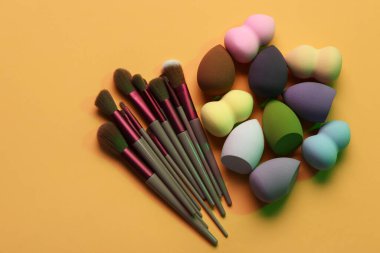 Turuncu arka planda makyaj süngerleri ve fırçalar