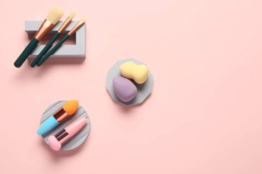 Pembe arka planda makyaj süngerleri ve fırçaları olan dekoratif podyumlar