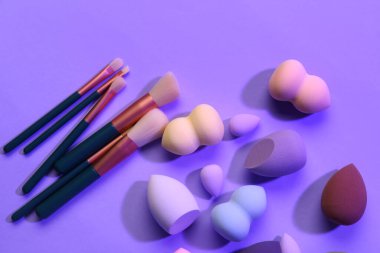 Leylak arka planında makyaj süngerleri ve fırçalar