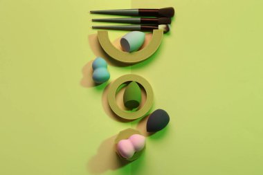 Yeşil arka planda makyaj fırçaları ve süngerleri olan dekoratif podyumlar