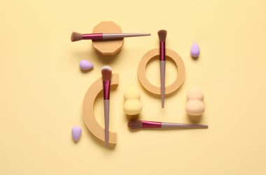 Sarı arka planda makyaj fırçası ve süngeri olan dekoratif podyumlar