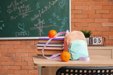 Sınıfın masasında kitap ve portakallarla süslü okul çantası.