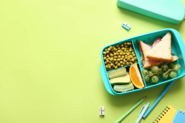 Lezzetli yemekleri ve yeşil arka planda farklı kırtasiyeleri olan bir beslenme çantası.