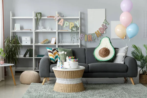 Interior of living room with birthday cake, balloons and pinata on grey sofa