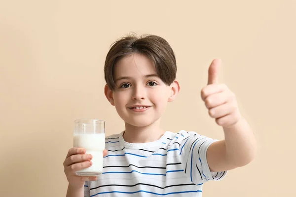 ベージュの背景に親指のジェスチャーを示すミルクのガラスを持つ小さな少年 — ストック写真